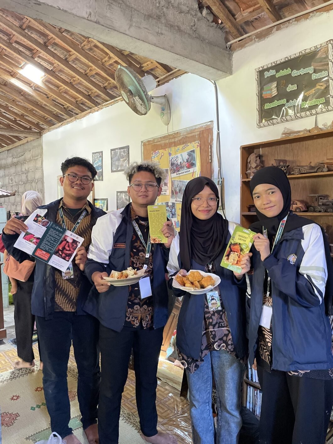 Mahasiswa KKN-T Tim 133 Saintek Kelompok 2 menunjukkan hasil produk dari demonstrasi masak berupa nugget sayur dan ekado yang diolah dari bahan ikan serta brosur penjelasan sosis daging merah dan muffin omelet sayur. (Sumber: Dokumentasi Pribadi).